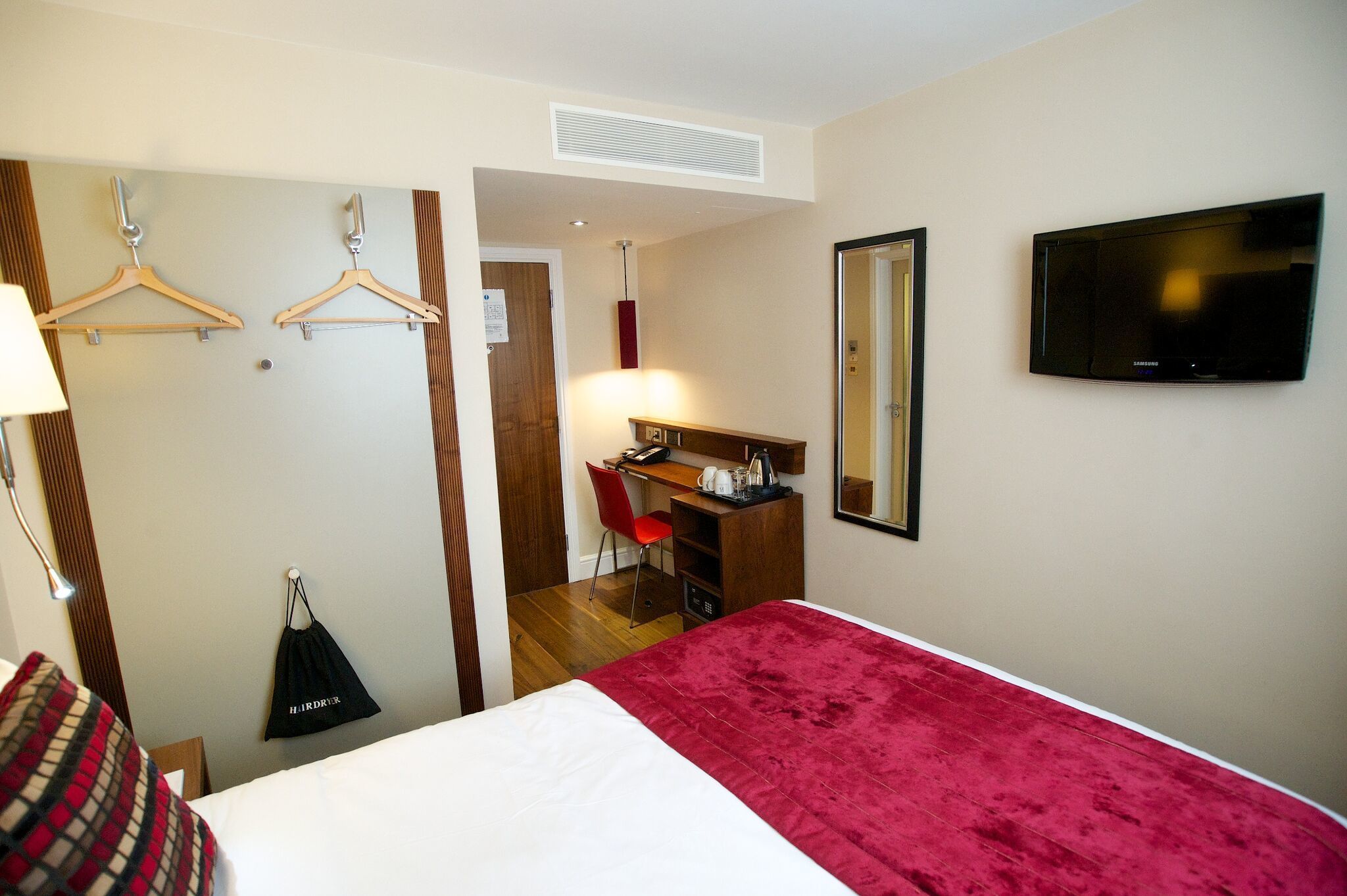 A hotel room with a bed, a desk with a chair, a TV, and a coat rack.