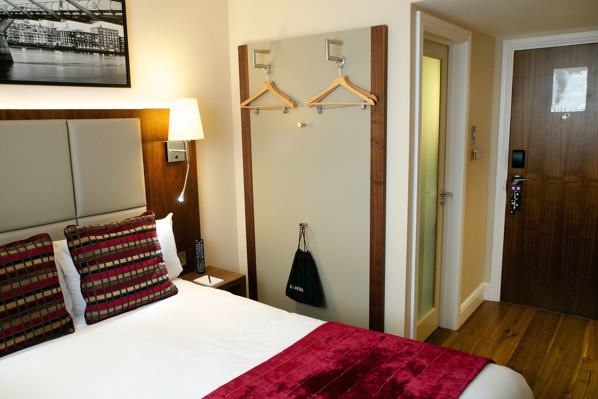 A hotel room with a bed, a nightstand, a lamp, a wardrobe, and a door.