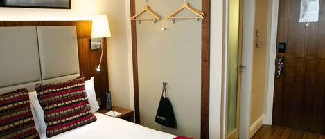 A hotel room with a bed, a nightstand, a lamp, a wardrobe, and a door.