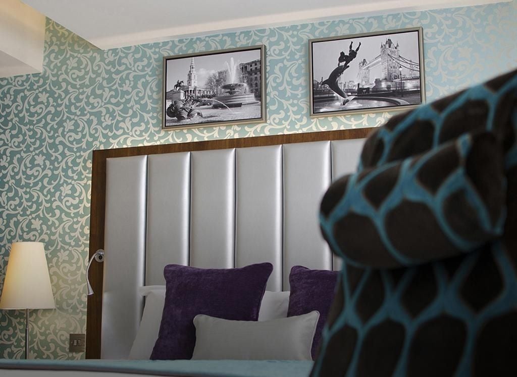 A bedroom with a bed, a headboard, a lamp, and two framed pictures on the wall.