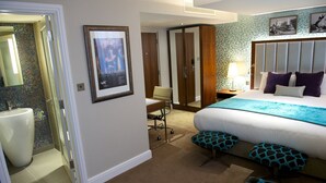 A hotel room with a large bed, a desk, and a chair. There is a bathroom with a toilet and a sink. - The Belgrave (London)