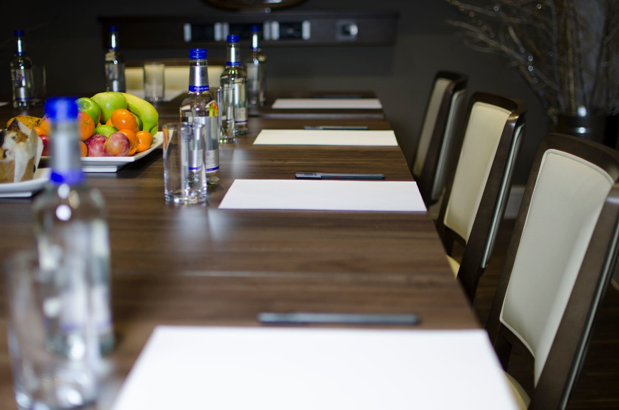 A conference room with a long table, chairs, water bottles, a fruit plate, and a pen.