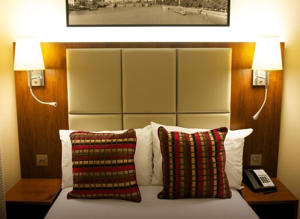A hotel room with a bed, two nightstands, a telephone, and a framed picture above the bed.