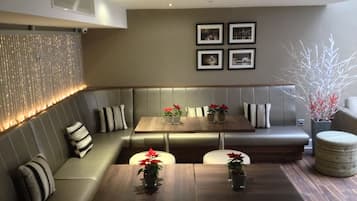 A modern dining area with a wooden table, cushioned seating, and decorative plants.