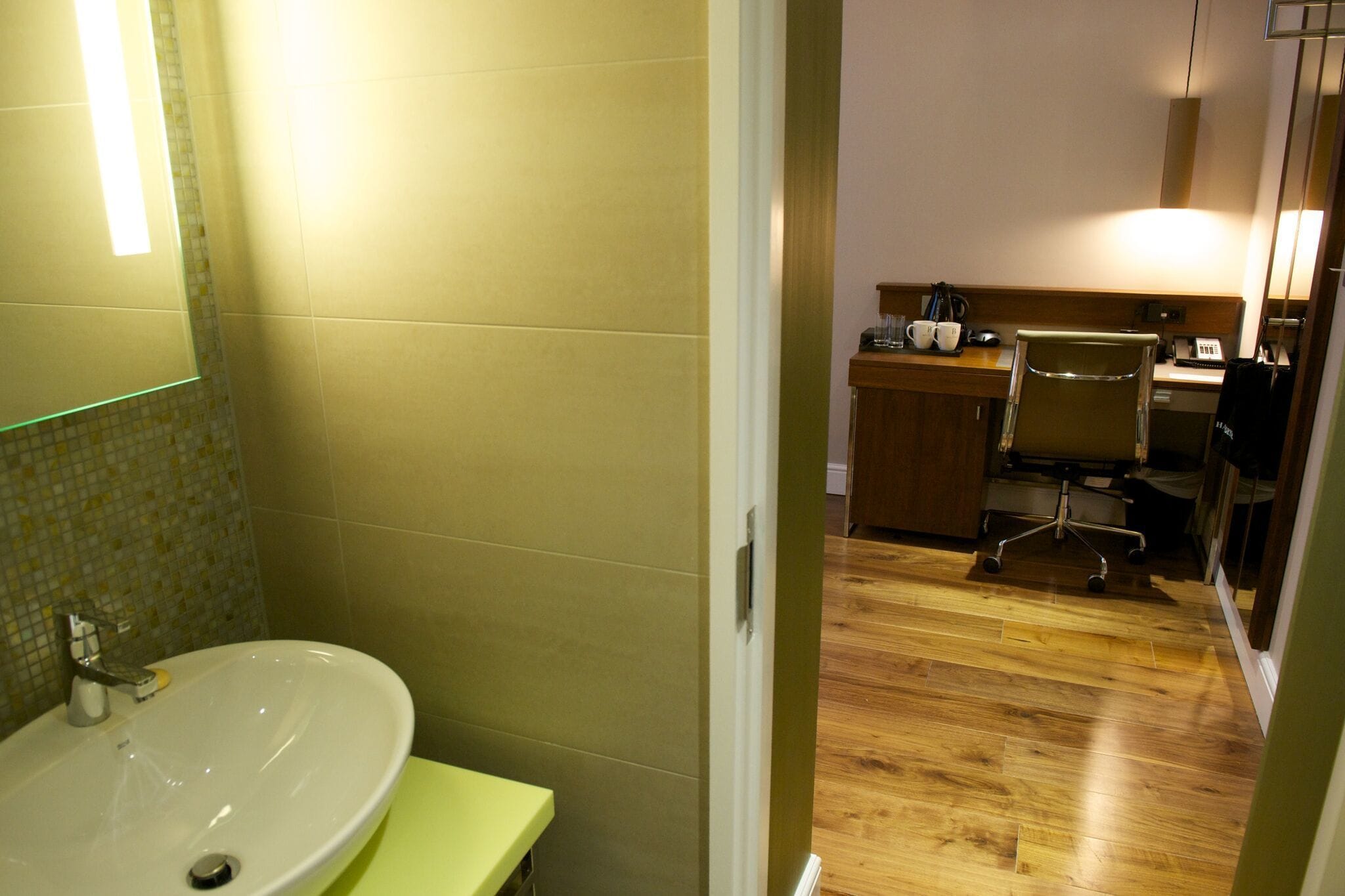 A hotel bathroom with a sink, mirror, and wooden floor.