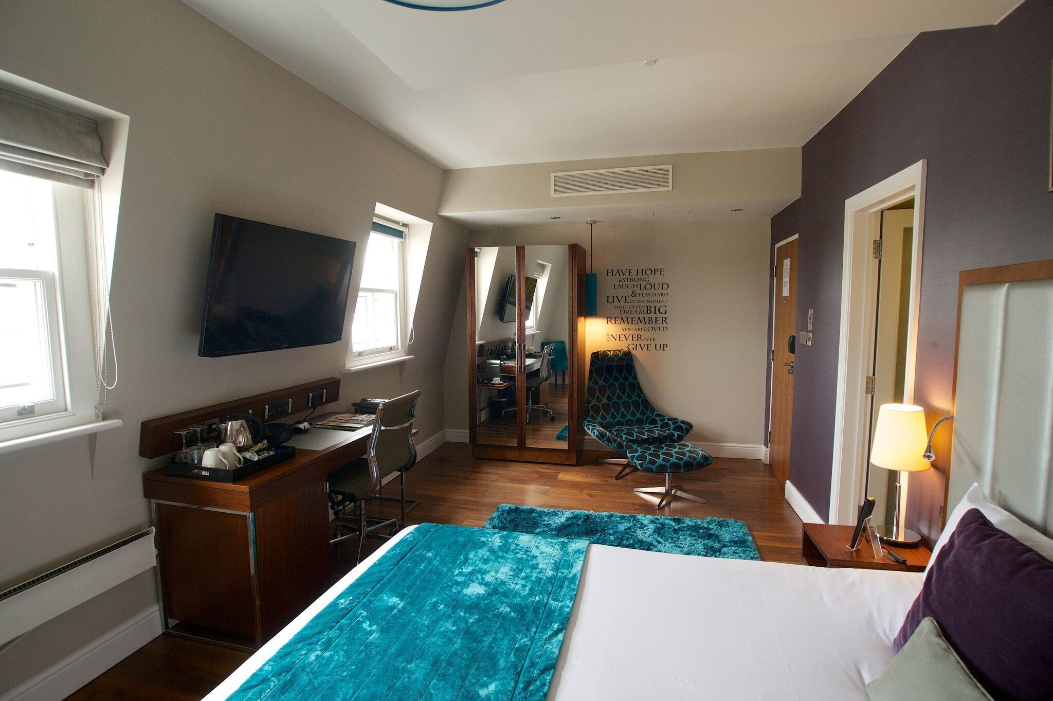 A hotel room with a bed, a desk, a chair, a TV, and a mirror.