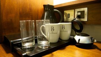A tray with two glasses and two mugs on a wooden surface, a black electric kettle, and a power outlet.