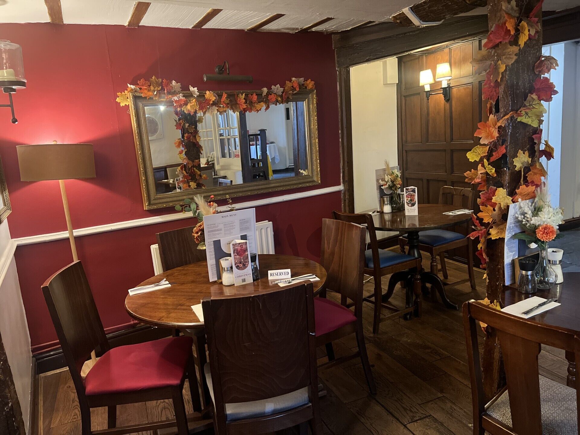 Interior de restaurante con mesas y sillas de madera, un espejo con hojas otoñales y un atril para el menú.