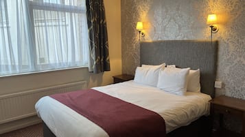 Ein Hotelzimmer mit einem Bett, zwei Nachttischlampen, einem fensterbelaubten Fenster und einem Wandteppich mit Muster.