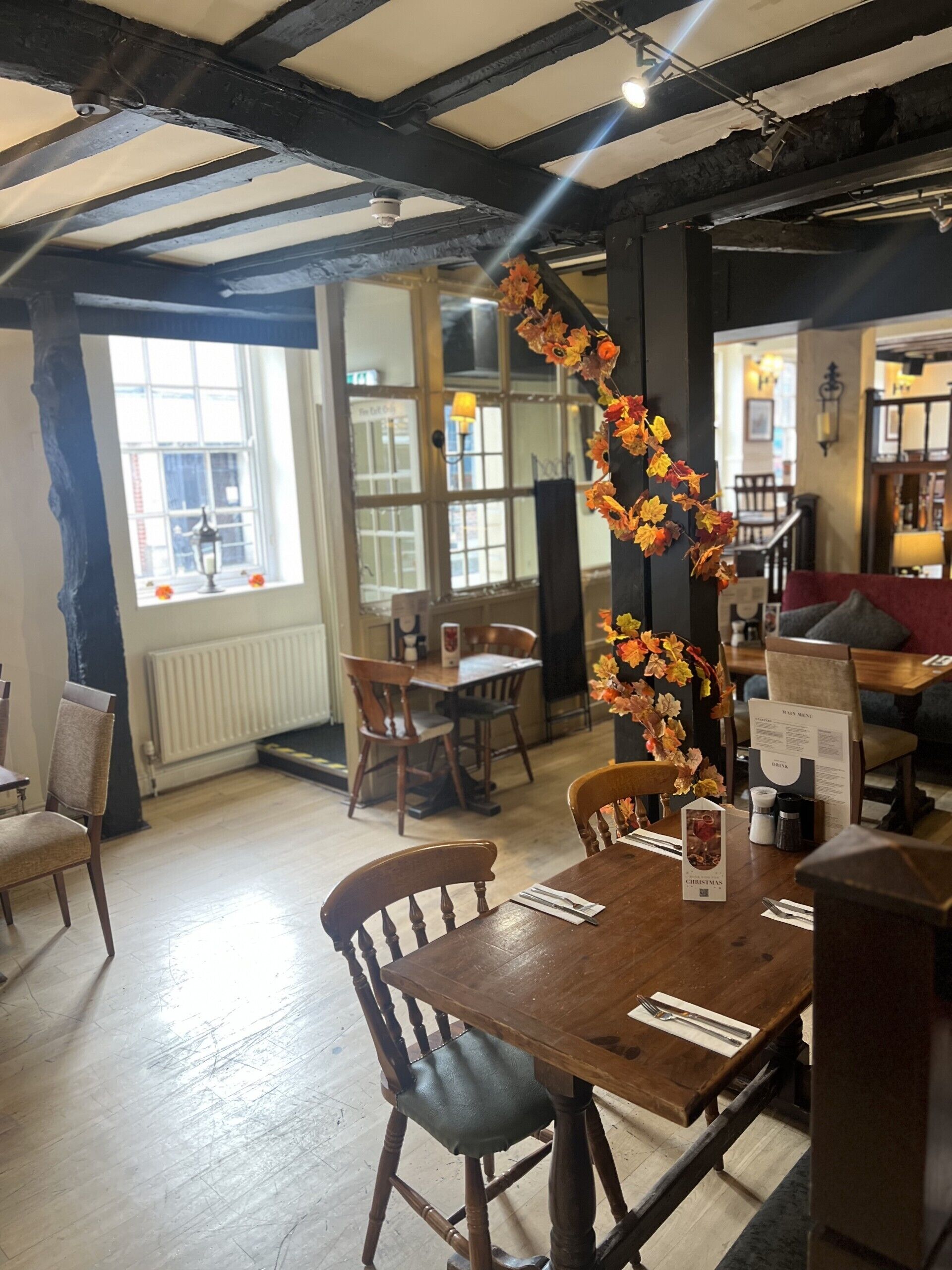 A restaurant interior with wooden tables and chairs, a decorative autumn leaf garland, and a menu stand.