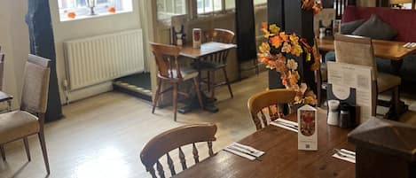 A restaurant interior with wooden tables and chairs, a decorative autumn leaf garland, and a menu stand.