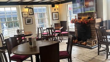 A restaurant with wooden floors, tables with chairs, a fireplace with seasonal decorations, and framed pictures on the walls.