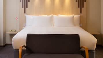 Habitación de hotel con una cama grande, una mesita de noche con lámpara, una silla y un teléfono instalado en la pared.