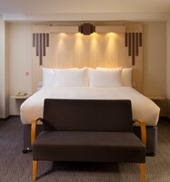 Ein Hotelzimmer mit einem großen Bett, einem Nachttisch mit Lampe, einem Sessel und einem an der Wand befestigten Telefon.