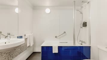 Une salle de bain équipée d’un lavabo, d’un miroir, d’une douche et de toilettes.