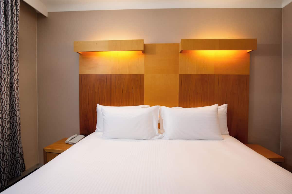 A hotel room with a large bed, two bedside tables, a telephone, and a headboard with built-in lighting.