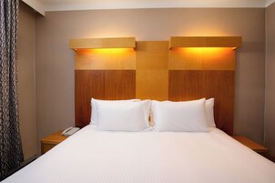 A hotel room with a large bed, two bedside tables, a telephone, and a headboard with built-in lighting.