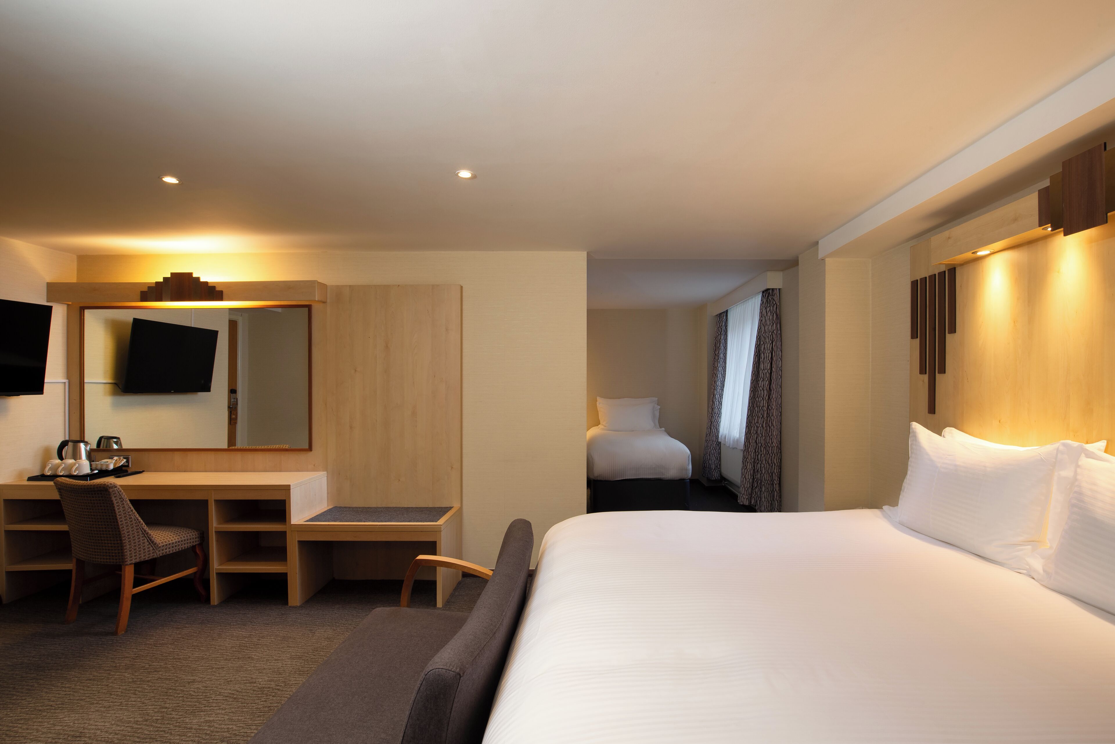Une chambre d’hôtel avec un grand lit, un bureau avec une chaise, un téléviseur à écran plat et un miroir.