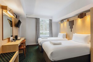 A hotel room with two beds, a desk with a chair, a flat-screen TV, and a window with curtains.