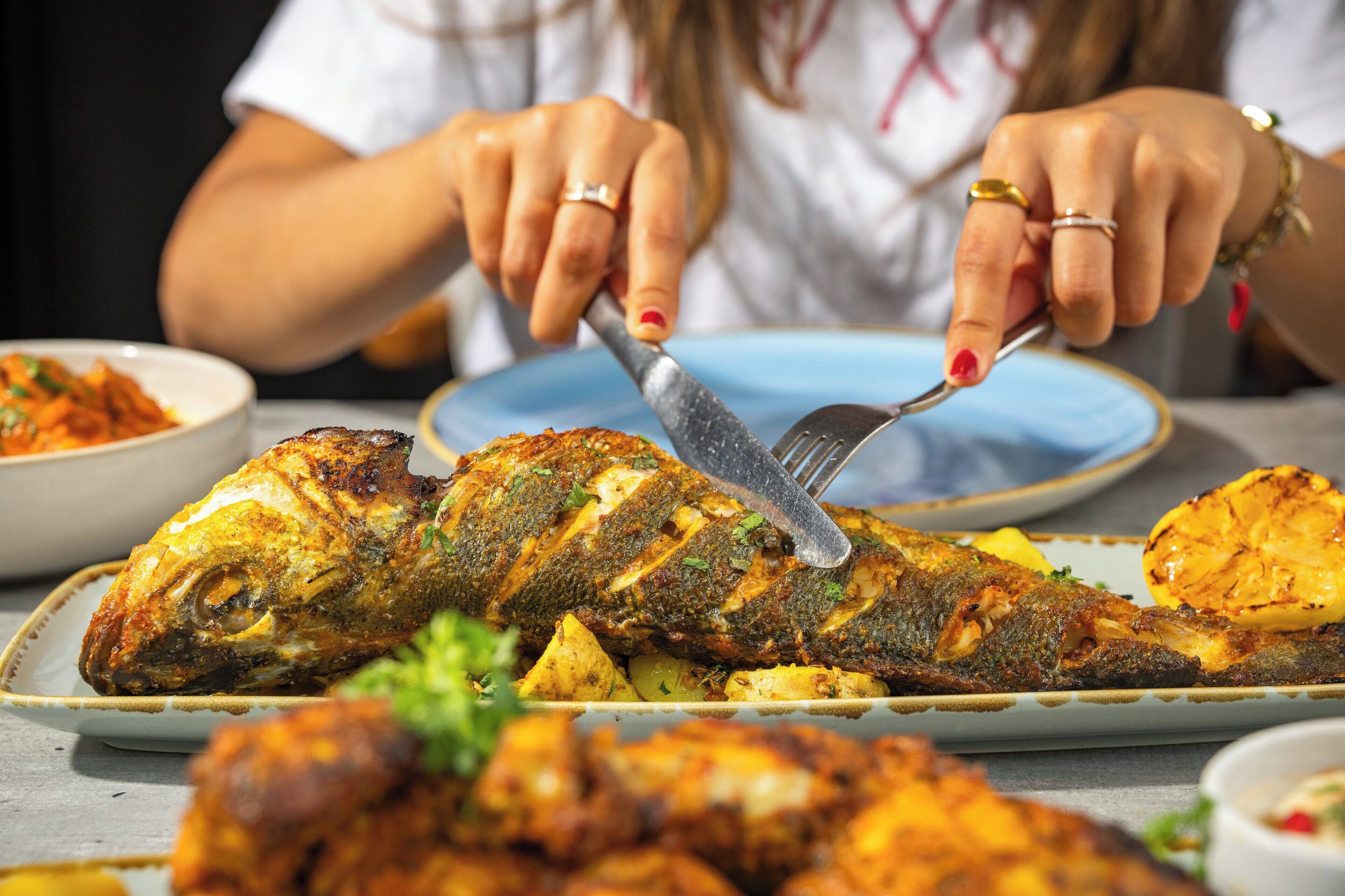 A person cutting a grilled fish on a plate.