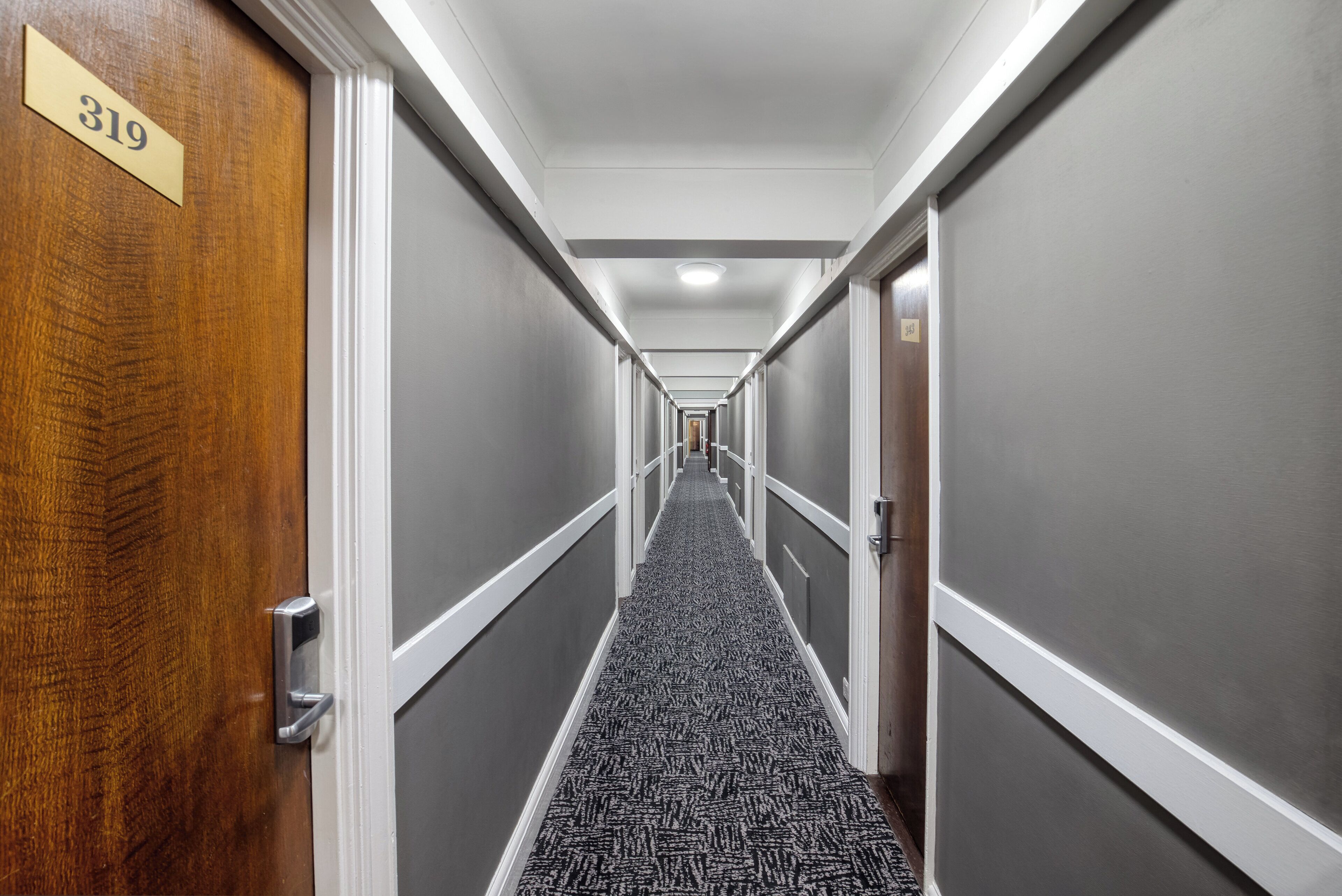 A hallway with doors numbered 319 and 320, carpeted with a geometric pattern, and white trim on the walls.