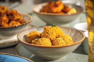 Eine Schüssel mit goldbraunen Speisen, möglicherweise Frittaten, garniert mit grünen Kräutern, auf einem Tisch mit weiteren Gerichten im Hintergrund.