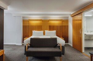 Ein Hotelzimmer mit Bett, Sessel, Kleiderschrank und einem Badezimmer mit Waschbecken.