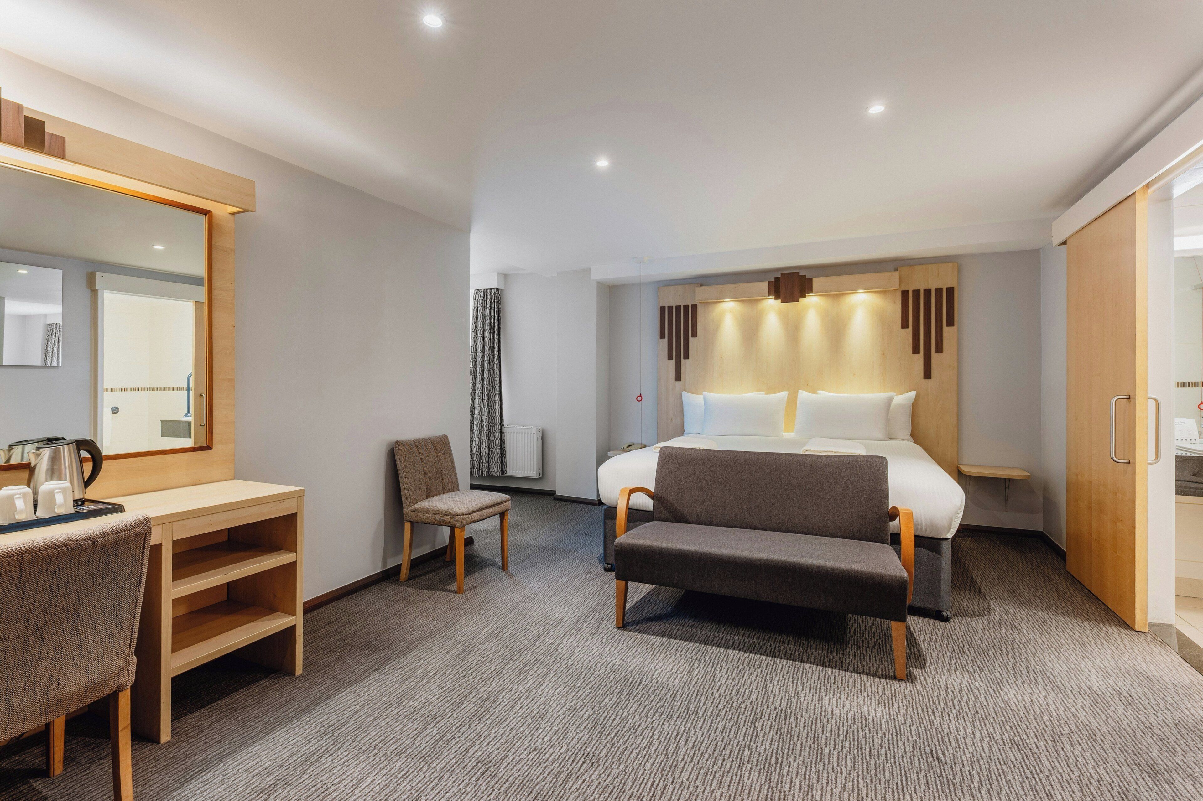 Ein Hotelzimmer mit einem Bett, einem Schreibtisch mit Stuhl, einem kleinen Tisch mit Wasserkocher und einem Kleiderschrank.