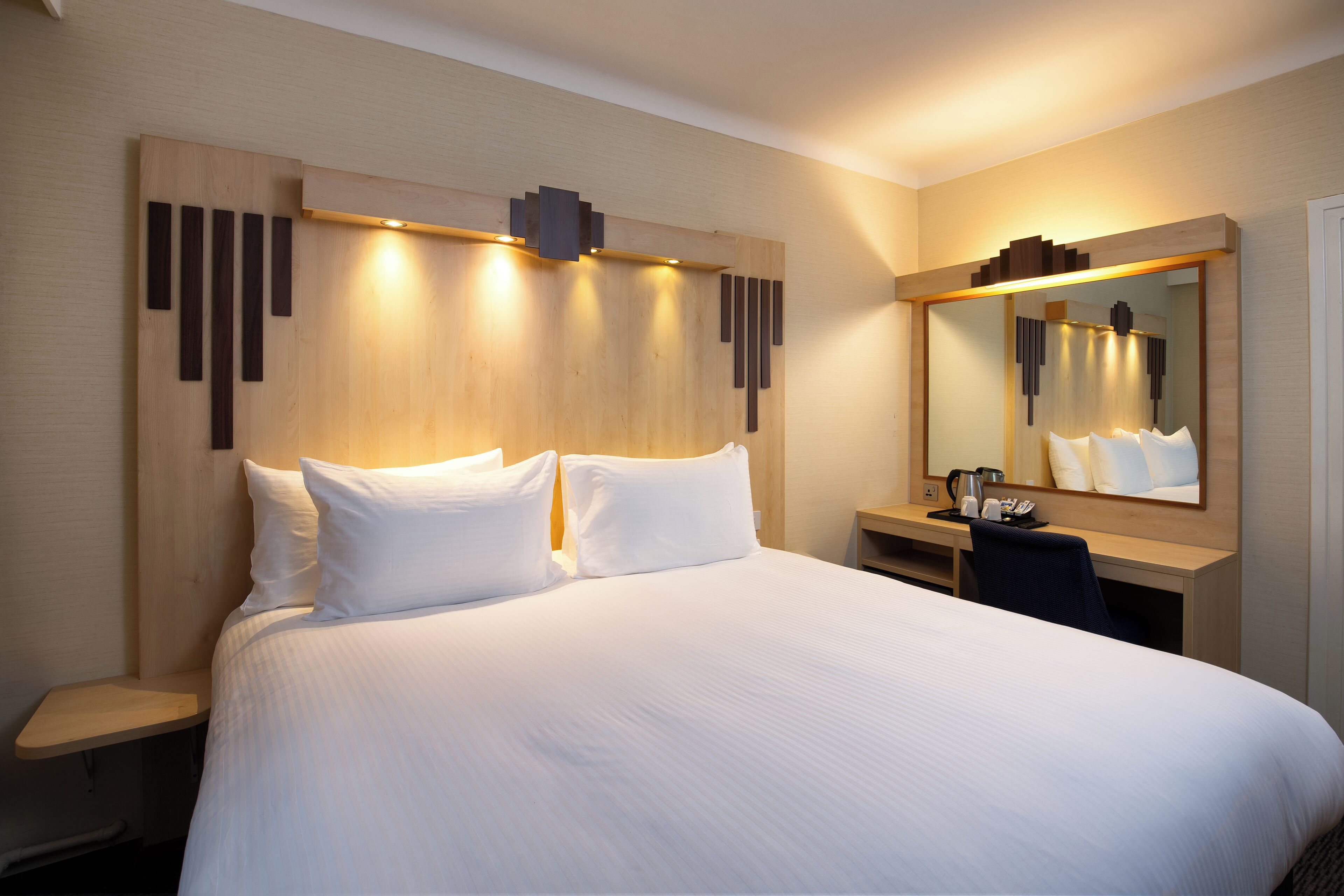 Una habitación de hotel con una cama grande, un escritorio, una silla y un espejo.