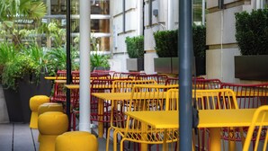 Outdoor seating with yellow tables and red chairs, surrounded by greenery and modern buildings. - Tavistock Hotel (London)
