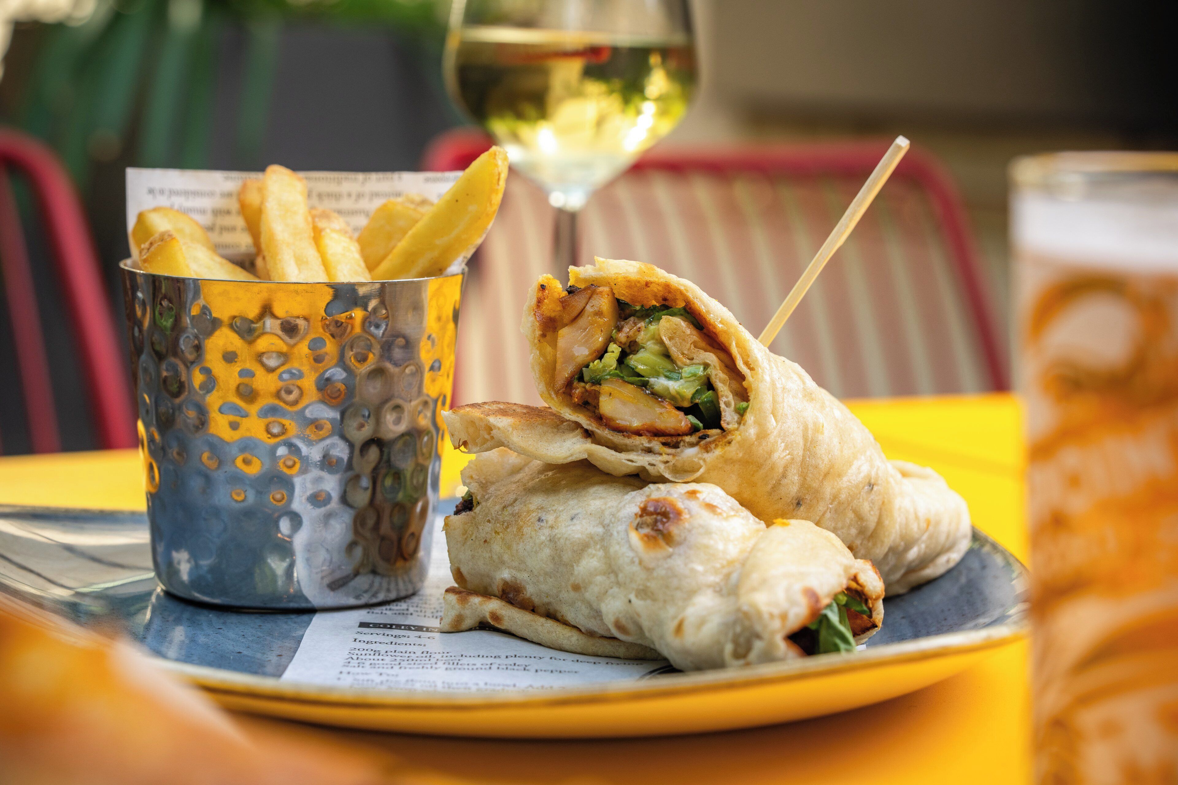 A meal consisting of a wrap, fries, and a glass of wine on a table with a menu.