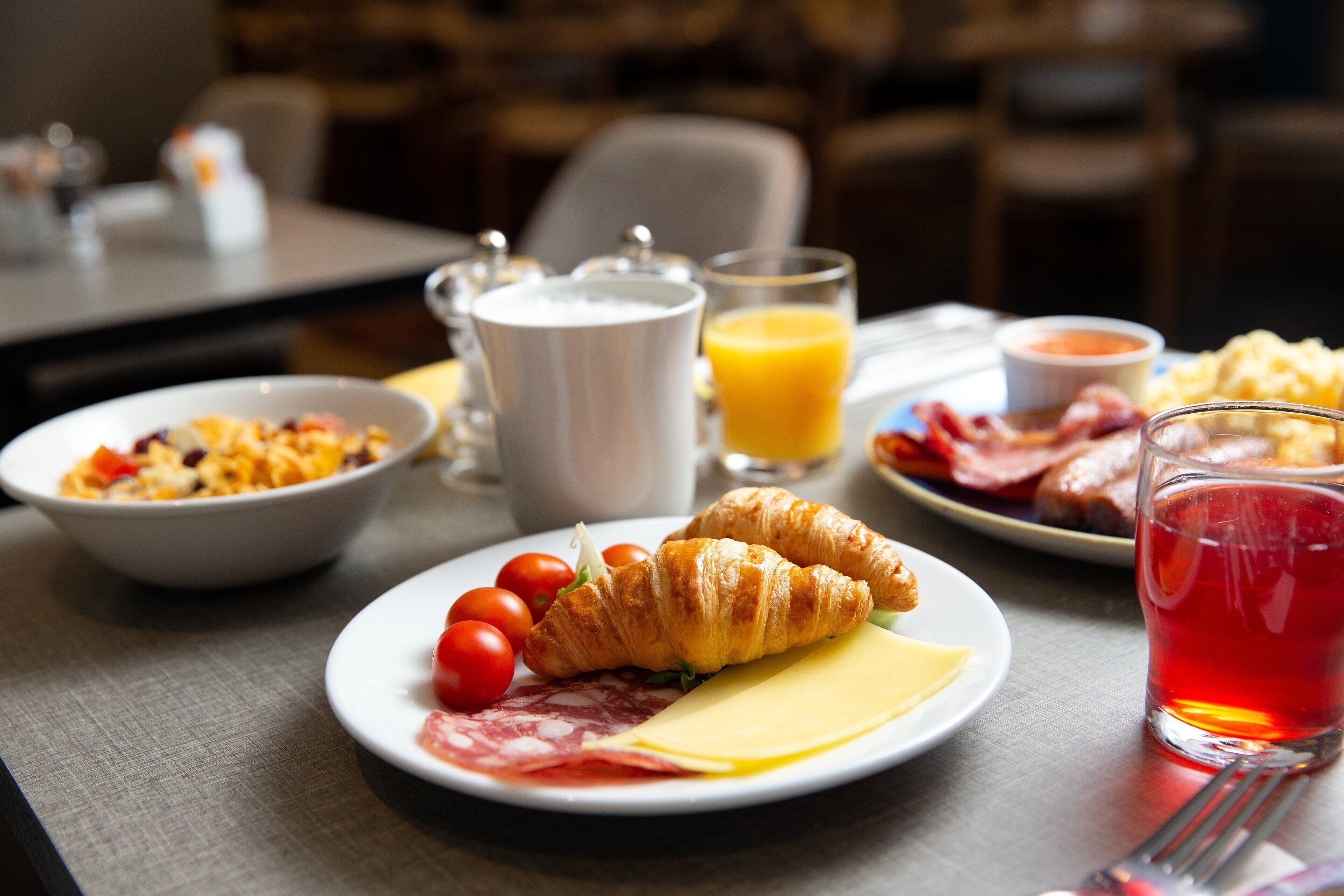 A breakfast setting with croissants, tomatoes, cheese, and a glass of red juice on a table.