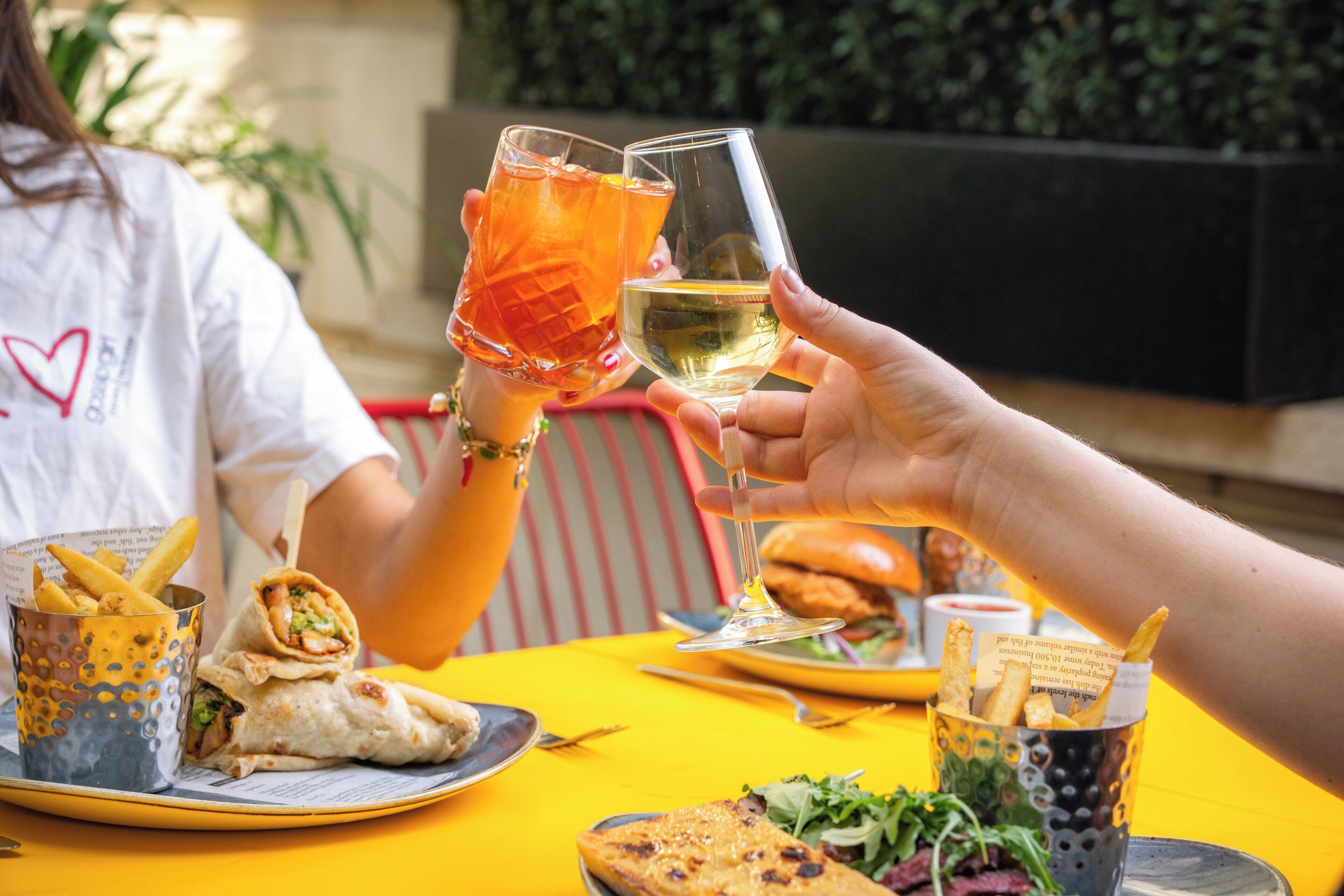Una mesa de comedor con comida y bebidas, incluyendo un sándwich, papas fritas y una bebida en un vaso.