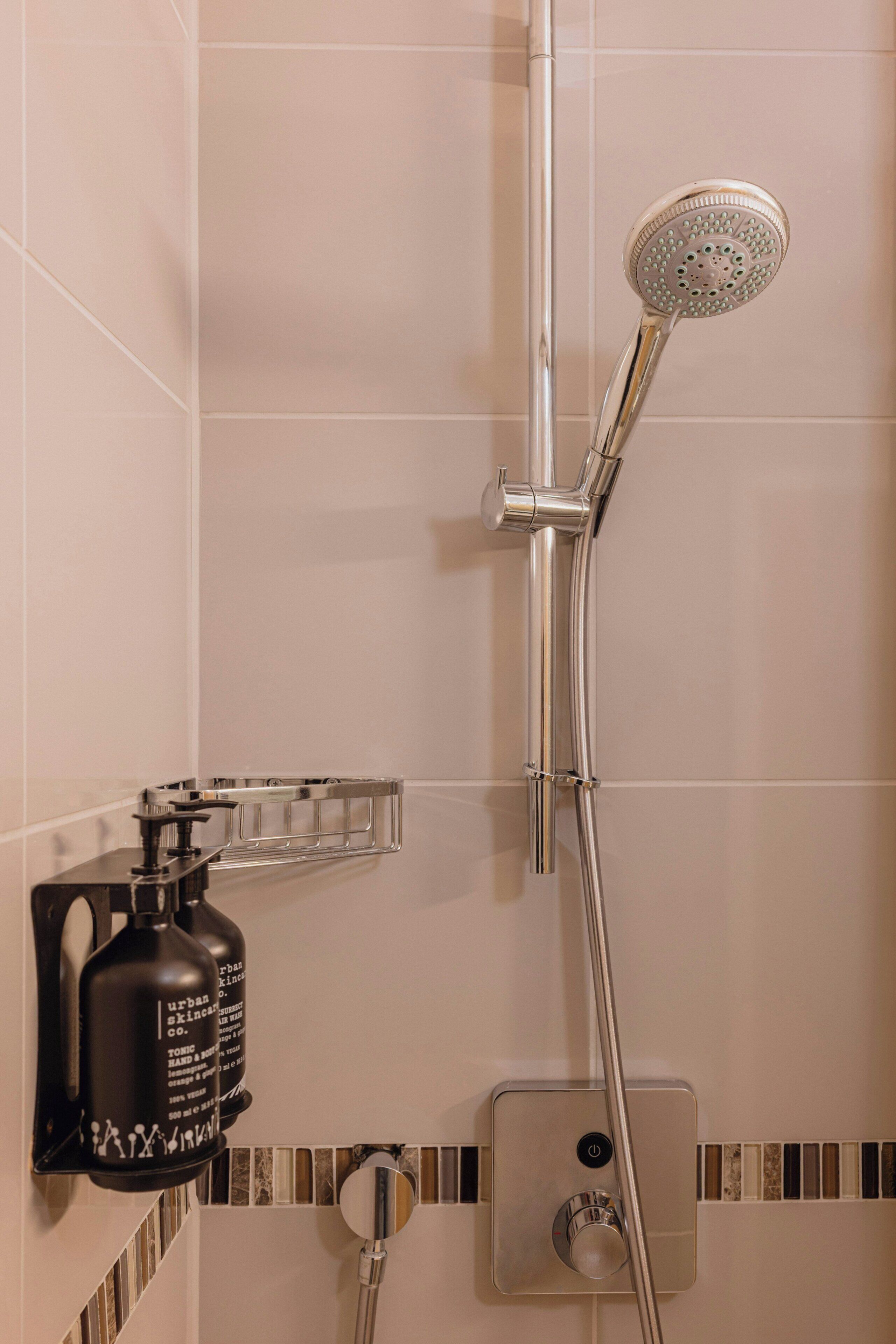 Een douche met een handdouche, een zeepdispenser aan de muur en een bedieningspaneel.