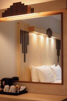 A hotel room with a large mirror, a bed with white linens, a bedside table with a coffee maker, and a tray with cups.