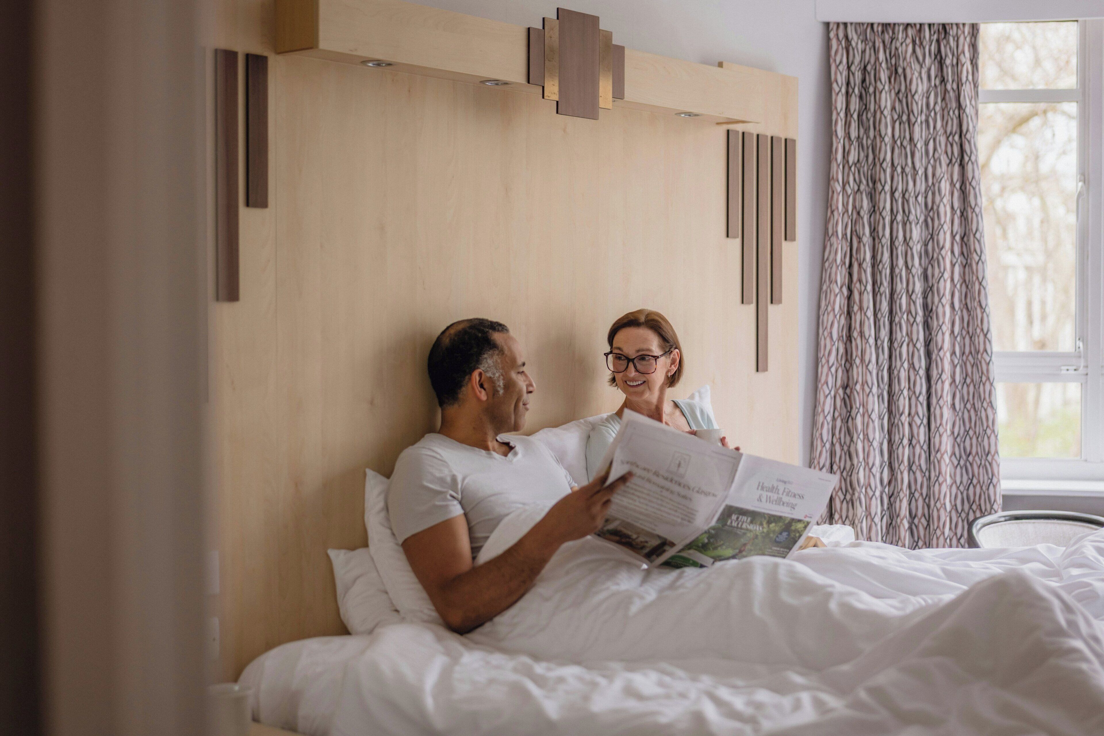 A bedroom with a wooden headboard, a window with curtains, and a bed with white bedding.