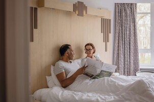 Een slaapkamer met een houten hoofdbord, een raam met gordijnen, en een bed met witte beddengoed.