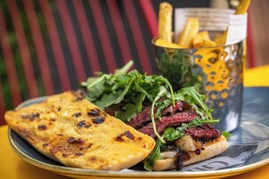 Ein Teller mit einem gegrillten Käse-Sandwich, einem Burger mit Salatbeilagen und einem Bierglas mit Pommes.