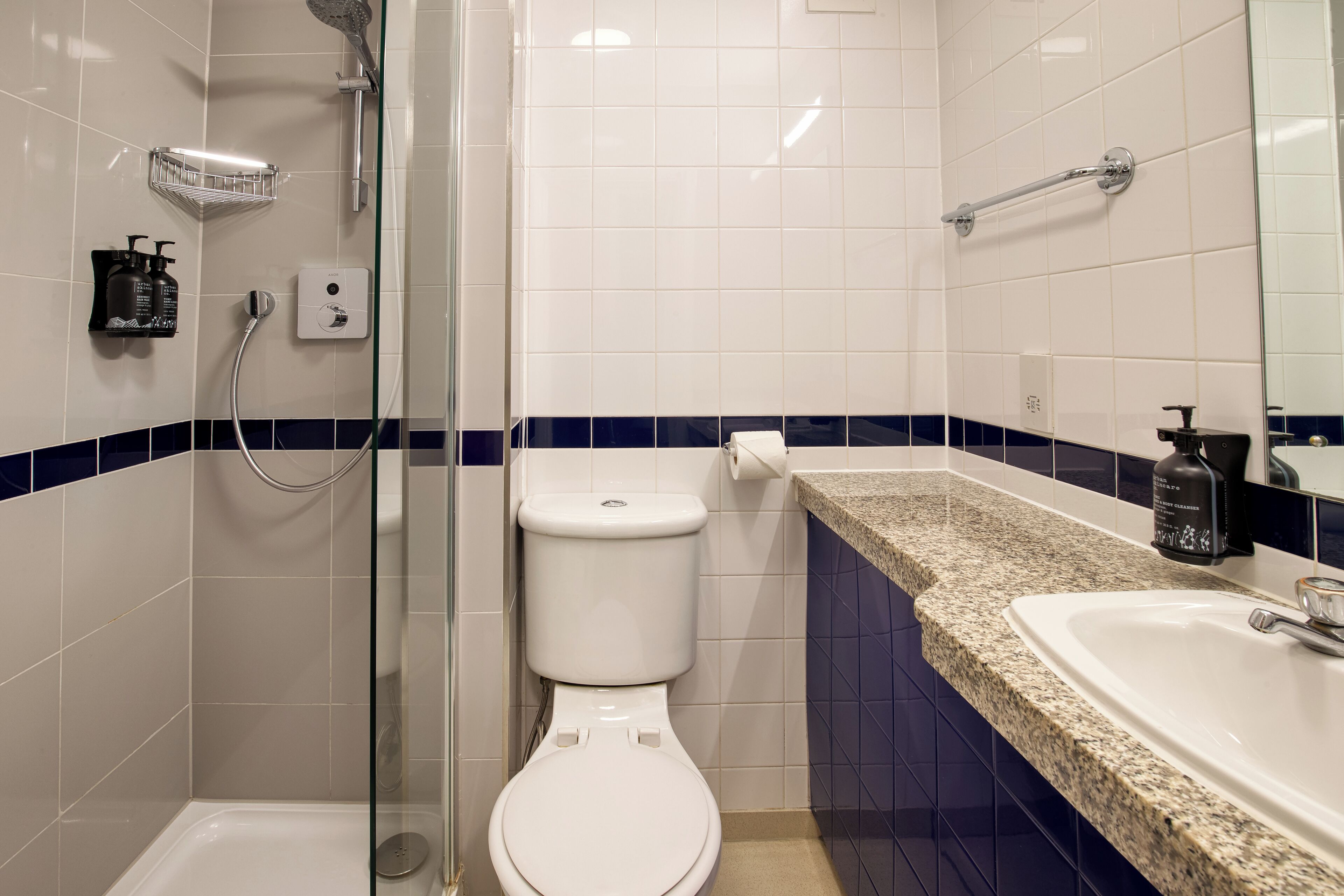 A bathroom with a white toilet, a glass-enclosed shower, a sink with a granite countertop, and a mirror.