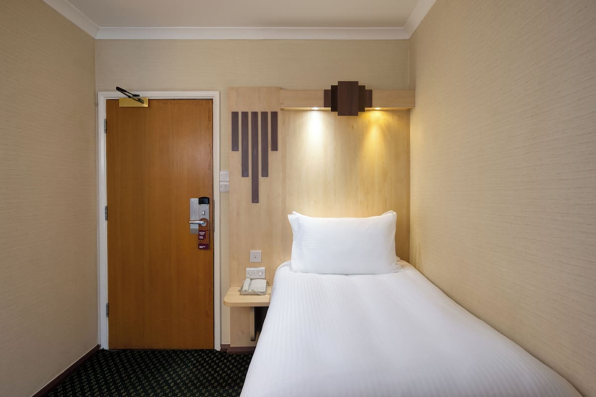 A hotel room with a wooden door, a bedside table with a phone, and a bed with white bedding.