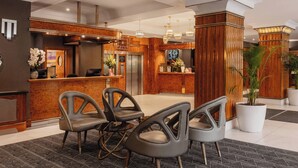 A hotel lobby with a reception desk, modern chairs, a large potted plant, and a visible elevator. - Tavistock Hotel (London)