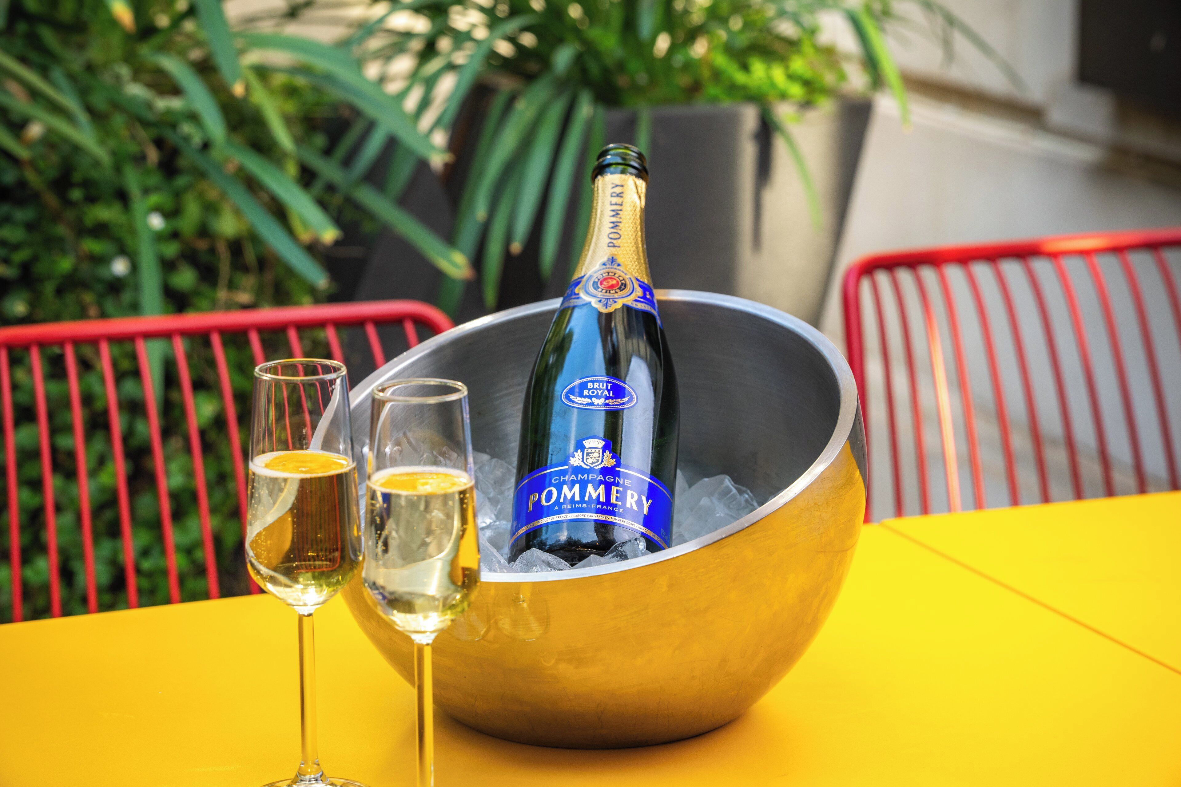 A bottle of champagne in a bowl on a yellow table with two glasses.