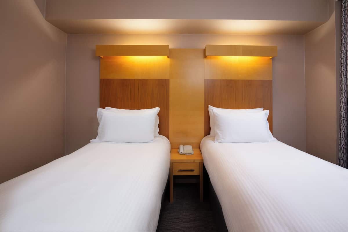 A hotel room with two single beds, wooden headboards, bedside tables with lamps, and a telephone.