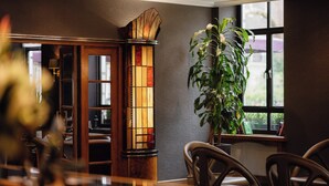 A room with a wooden cabinet, a large potted plant, and a window with a view. - Tavistock Hotel (London)
