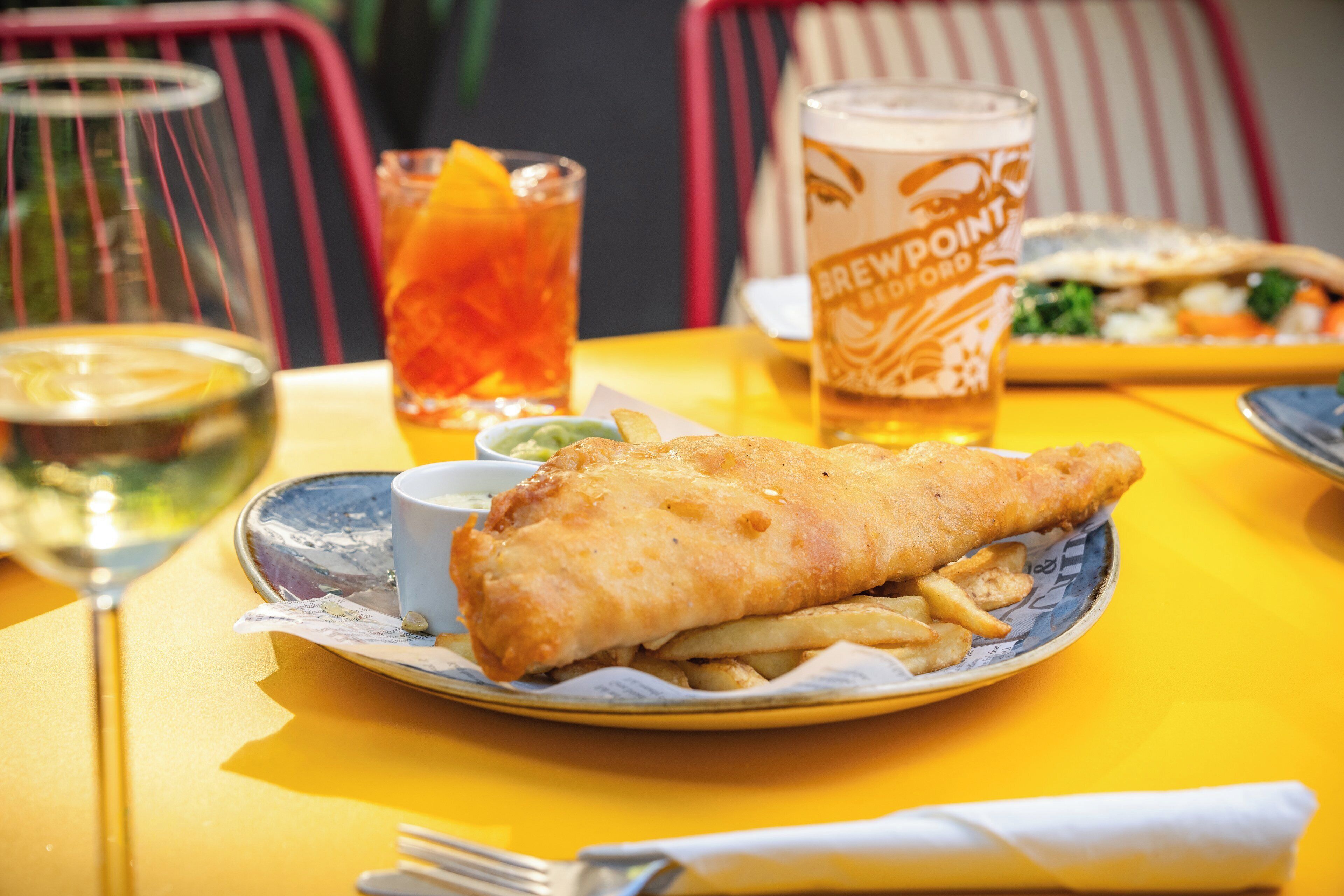 Ein Tisch mit einer Fisch-und-Chips-Kombination, einem Glas Bier und einem Glas Orangensaft.