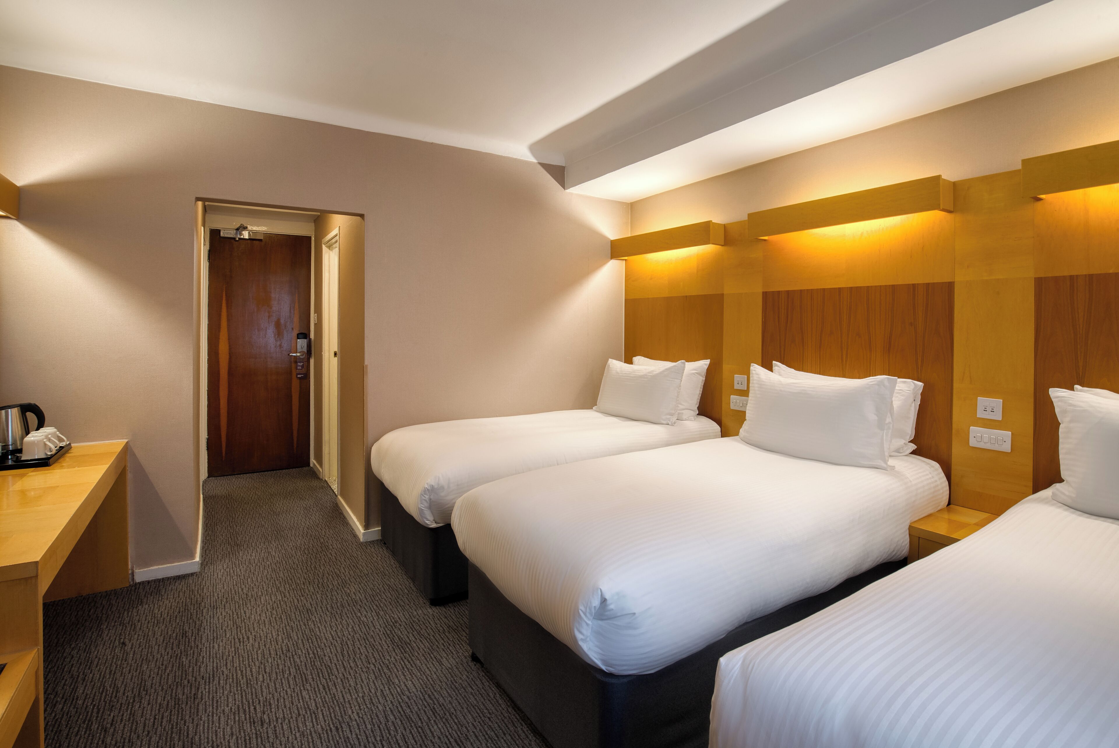 A hotel room with two beds, a wooden headboard, a desk with a telephone, and a door leading to another room.