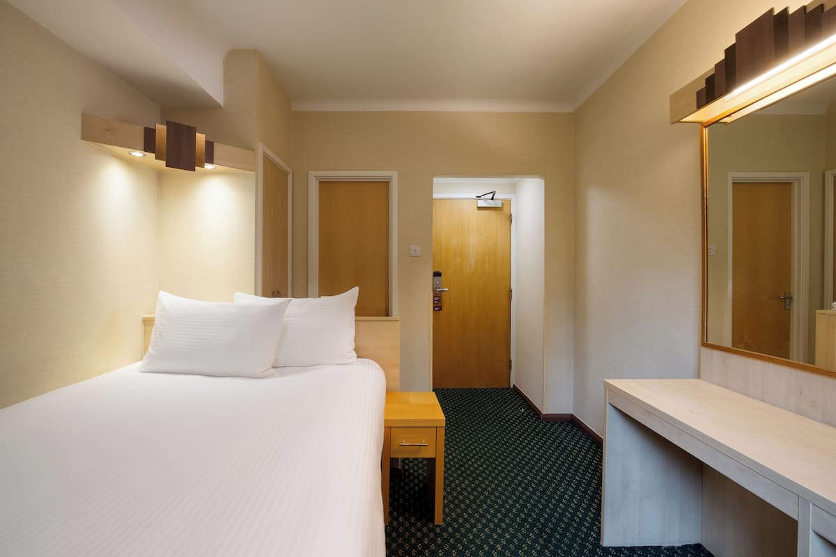 A hotel room with a bed, bedside table, mirror, and a door leading to another room.