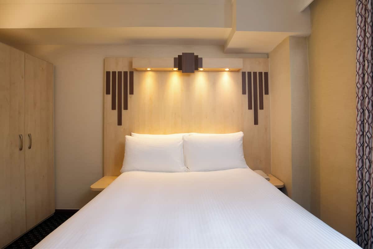 A hotel room with a large bed, wooden headboard, and a built-in shelf with lights.