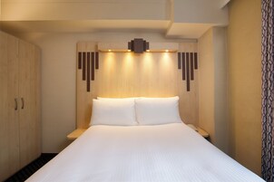 A hotel room with a large bed, wooden headboard, and a built-in shelf with lights.