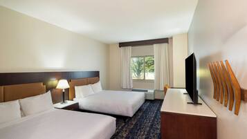 A hotel room with two beds, a desk, a TV, and a window with curtains.